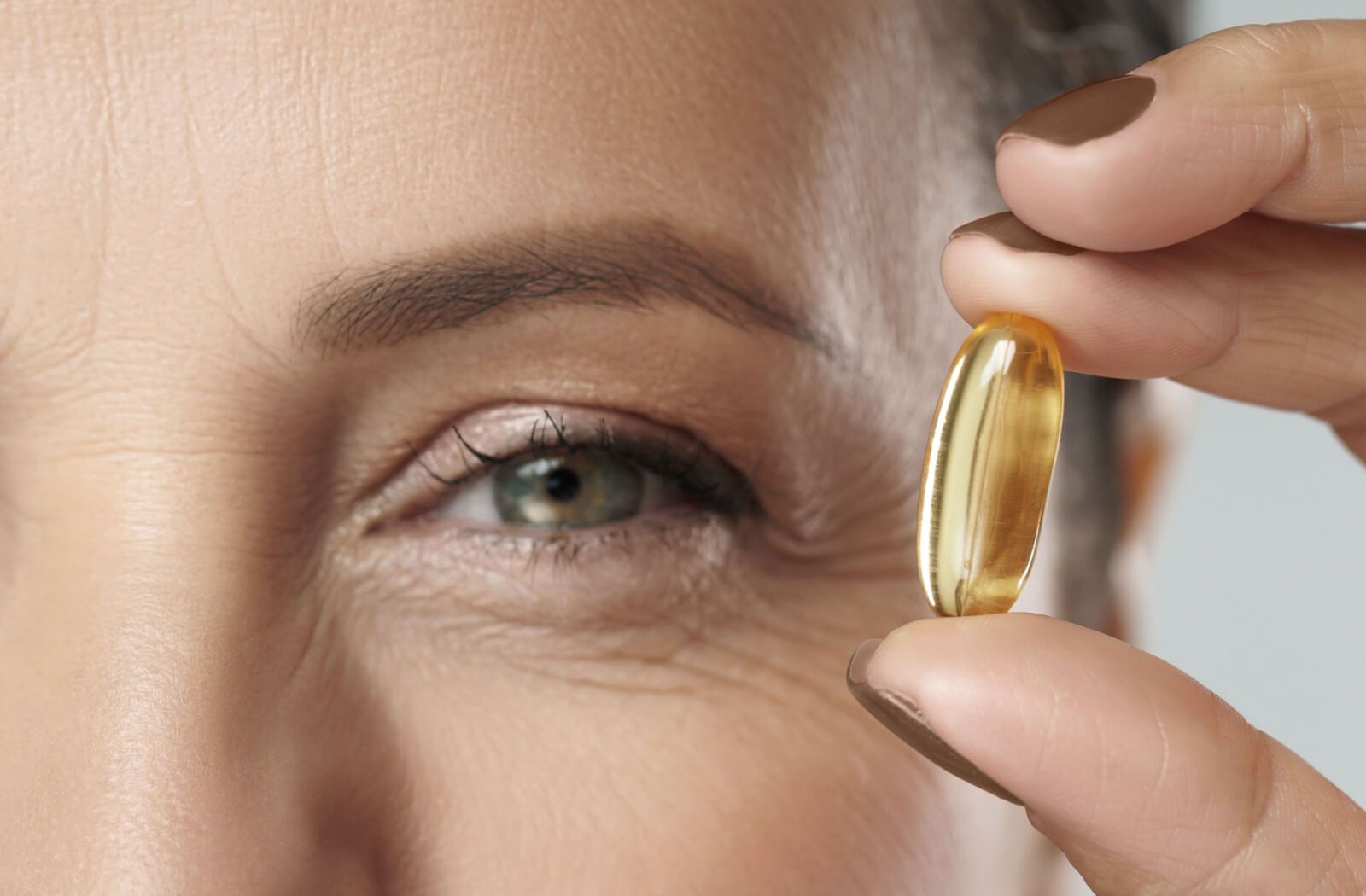 A close-up eye of a middle-aged woman holding an omega-3 capsule.
